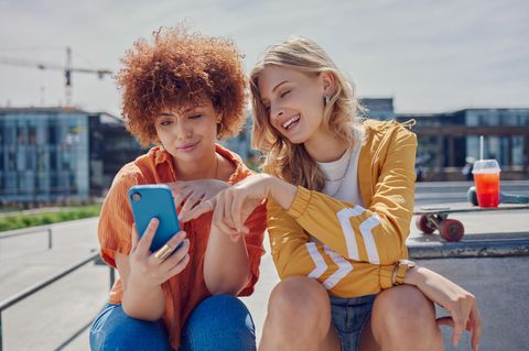 Zwei Freundinnen schauen gemeinsam ins Handy und freuen sich über den CallYa-Jahrestarif.