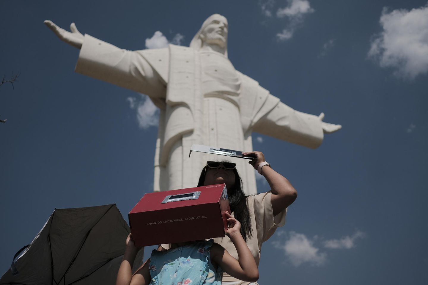 Eine Frau und ihre Tochter stehen vor Christusstatue beobachten die Sonnenfinsternis mit selbst gemachten Sonnenschutzmitteln.
