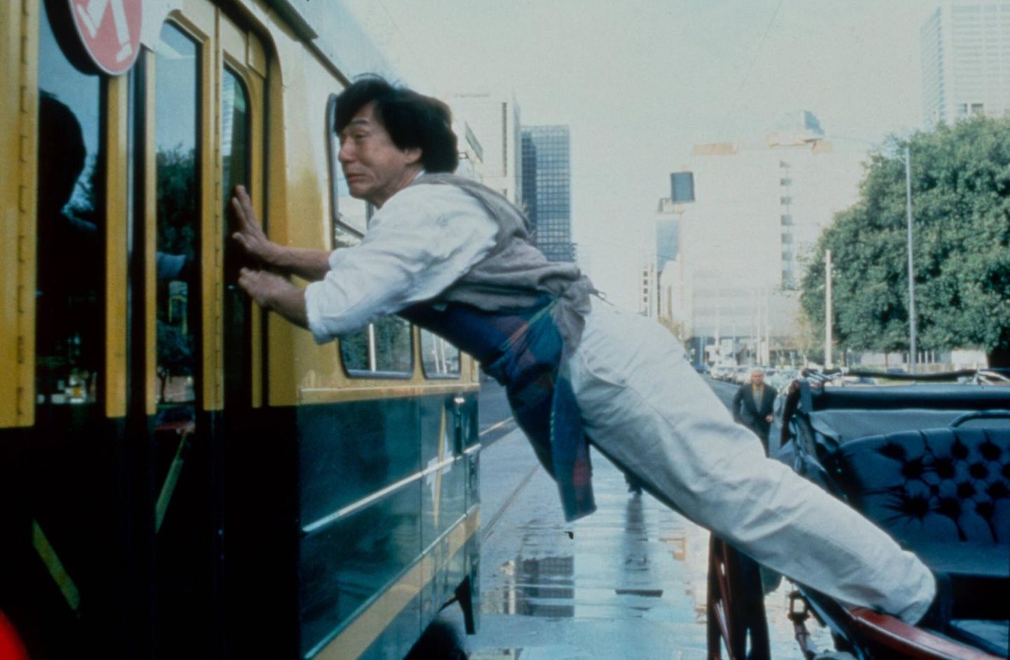 Jackie Chan hängt zwischen einem Zug und einem Auto Jackie Chan hängt zwischen einem Zug und einem Auto