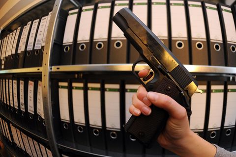 Eine Frau in der Waffenbehörde hält vor einem Aktenschrank eine Schusswaffe in der Hand