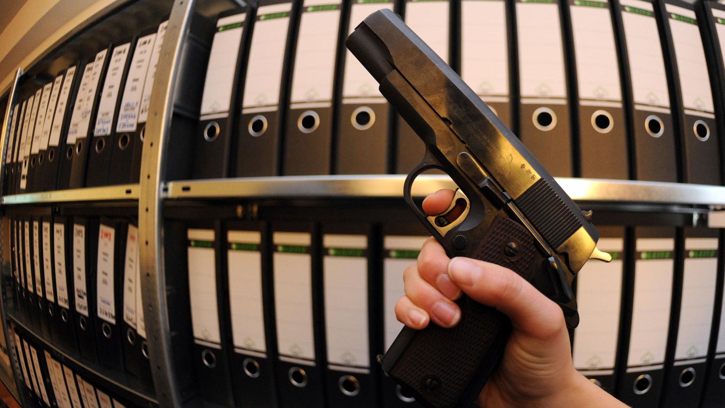 Eine Frau in der Waffenbehörde hält vor einem Aktenschrank eine Schusswaffe in der Hand