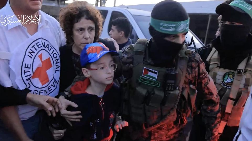 Een jonge Israëlische burger is vrij om te gaan.  Sein vermummter Peiniger der Hamas hält ihn im Arm