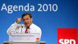 Gerhard Schröder steht am Rednerpult vor einer blauen Wand mit weißem "Agenda 2010"-Schriftzug