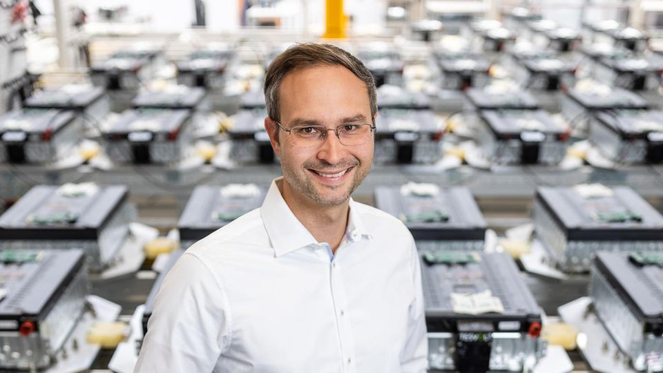 Ein Mann mit weißem Hemd steht in einer Fabrik für Batteriespeicher Ein Mann mit weißem Hemd steht in einer Fabrik für Batteriespeicher
