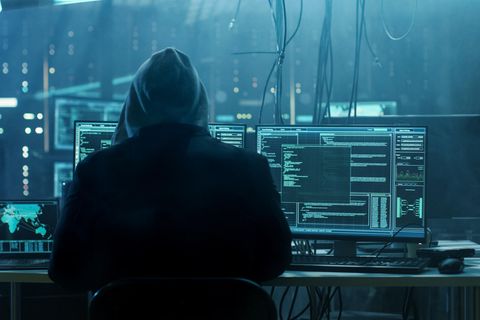 Ein Hacker sitzt in einem dunklen Raum voller Technik. Bereitet er einen Cyberangriff vor?