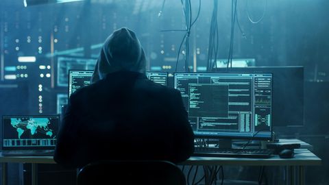 Ein Hacker sitzt in einem dunklen Raum voller Technik. Bereitet er einen Cyberangriff vor?