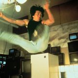 Jackie Chan springt mit im 90-Grad-Winkel angehobenen Beinen in die Luft