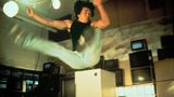Jackie Chan springt mit im 90-Grad-Winkel angehobenen Beinen in die Luft
