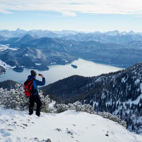 Ein winterlich gekleideter Wanderer blickt vom Berg auf einen See