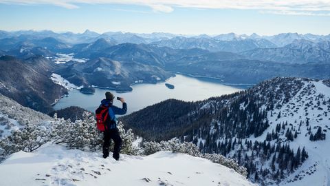 Ein winterlich gekleideter Wanderer blickt vom Berg auf einen See