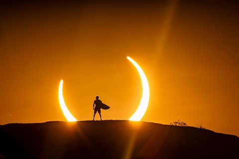 Mann mit Surfbrett vor Sonnenfinsternis