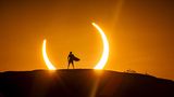 Mann mit Surfbrett vor Sonnenfinsternis