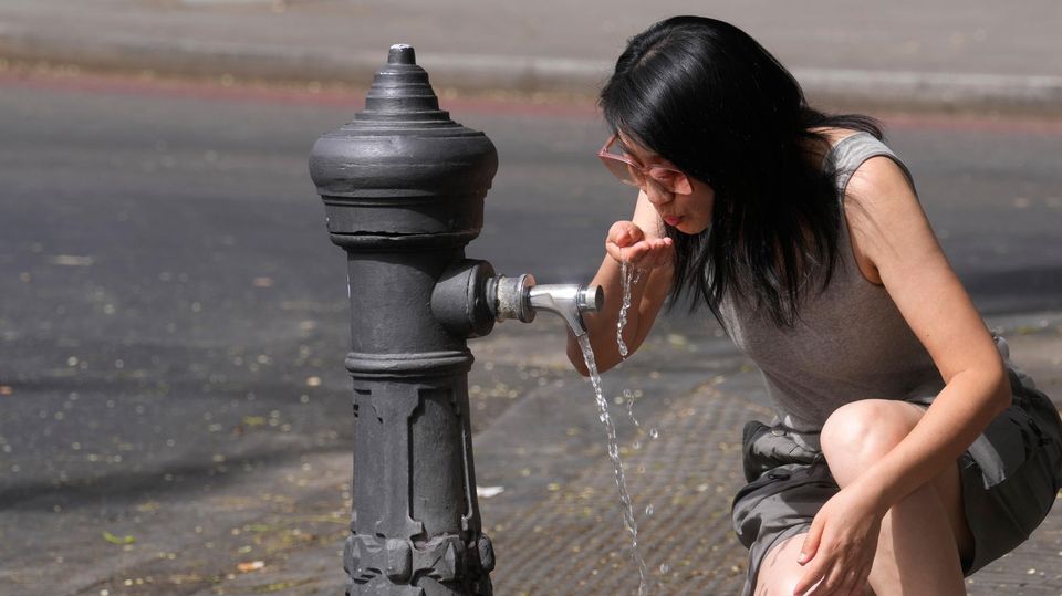 Eine Frau trinkt aus einem Wasserbrunnen.