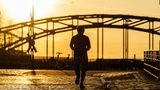Im Morgenlicht läuft ein Mann über Kopfsteinpflaster auf eine Brücke zu