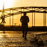 Im Morgenlicht läuft ein Mann über Kopfsteinpflaster auf eine Brücke zu