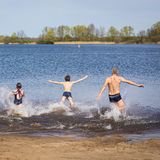 Eine vierköpfige Familie ist von hinten zu sehen, wie sie in einen Badesee läuft