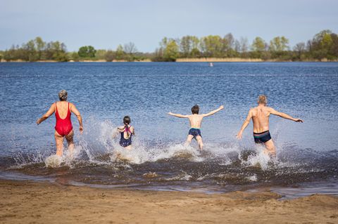 Eine vierköpfige Familie ist von hinten zu sehen, wie sie in einen Badesee läuft