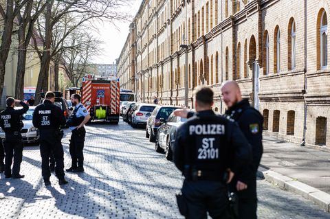 Polizisten und Feuerwehrleute stehen vor einem Wohnhaus in Halle an der Saale