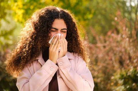Frau mit Allergie schnäuzt in ein Taschentuch.
