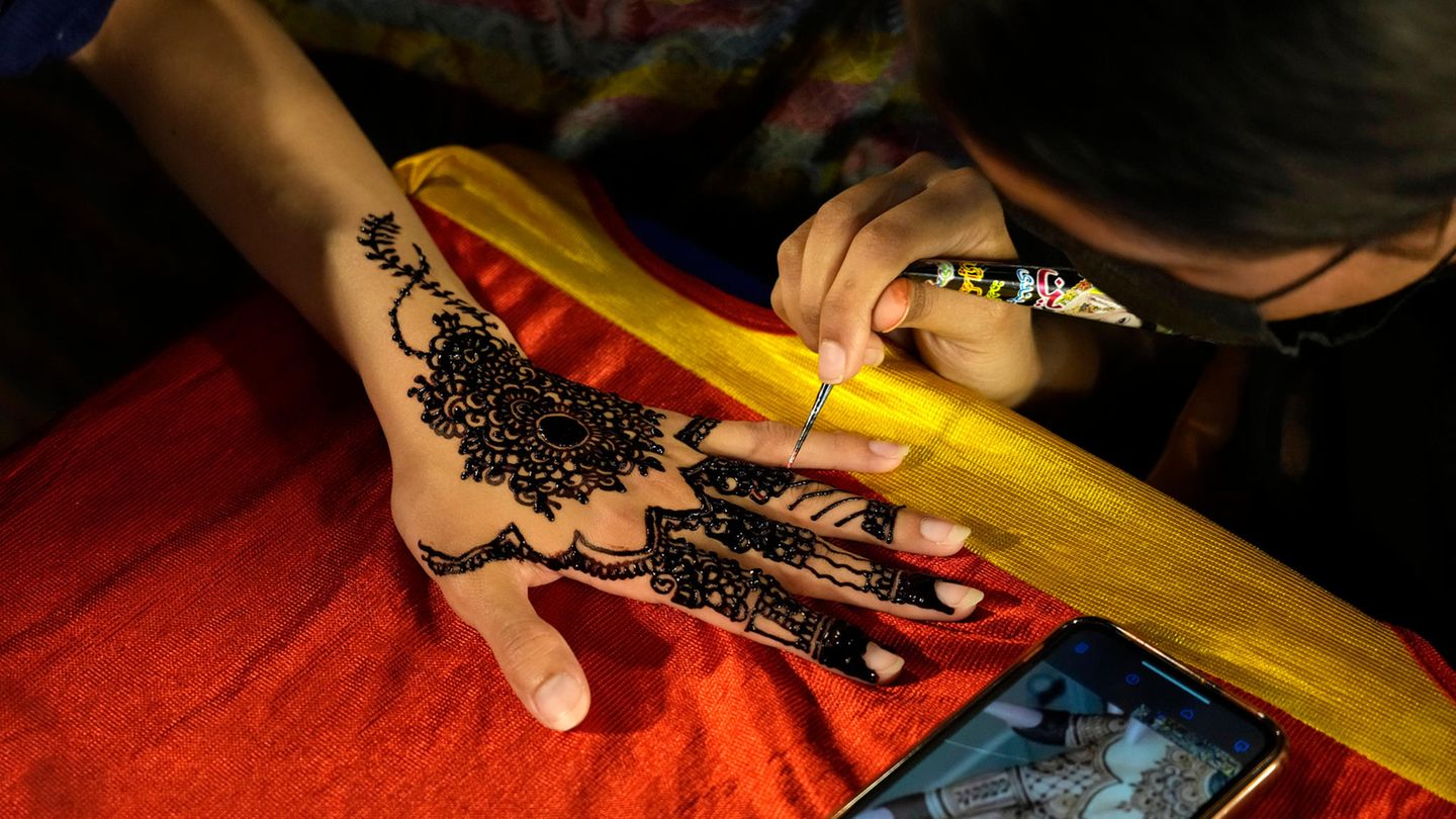 Eine Kosmetikerin verziert mit Henna die Hand einer Kundin mit traditionellen Mustern in Vorbereitung auf das bevorstehende Eid al-Fitr-Fest auf einem Markt in Lahore, Pakistan. Eid al Fitr markiert das Ende des islamischen heiligen Monats Ramadan