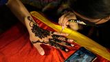 Eine Kosmetikerin verziert mit Henna die Hand einer Kundin mit traditionellen Mustern in Vorbereitung auf das bevorstehende Eid al-Fitr-Fest auf einem Markt in Lahore, Pakistan. Eid al Fitr markiert das Ende des islamischen heiligen Monats Ramadan