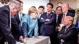 Angela Merkel lehnt sich über einen Tisch und redet mit Trump der stur auf einem Stuhl hockt