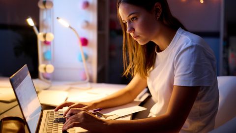 Eine Frau macht Überstunden und arbeitet abends vor ihrem Laptop
