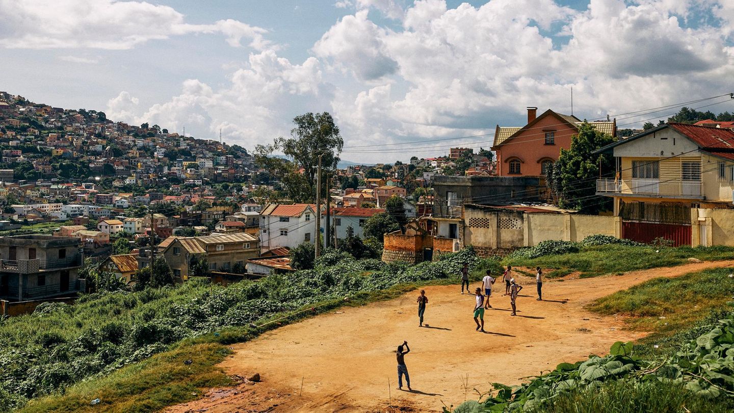 Kinder spielen auf einem Sandplatz. Im Hintergrund Häuser und Hügel