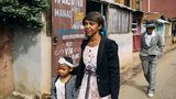 Eine Mutter läuft mti ihrer kleinen Tochter eine Straße entlang hinter ihr ein älterer Herr im grauen Anzug