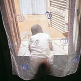 Ein Junge lehnt sich hinter einem Mückennetz aus dem geöffneten Fenster