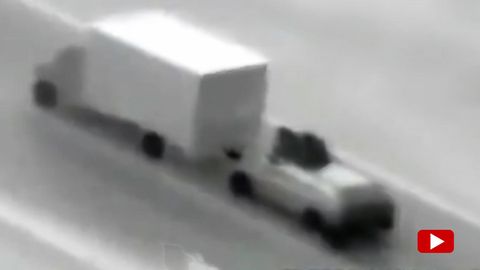 Zwei vermummte Personen sitzen auf einem Autodach hinter einem fahrenden Lastwagen