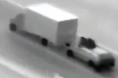 Zwei vermummte Personen sitzen auf einem Autodach hinter einem fahrenden Lastwagen