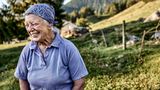 Ältere Sennerin steht vor ihrem Alm