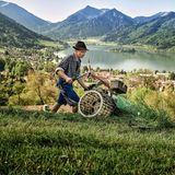 Junger Bauer mäht auf der Hangwiese