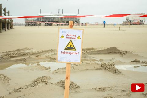Ein Warnschild mit der Aufschrift: "Achtung Treibsand Lebensgefahr!" steckt im Sand am Strand in St. Peter-Ording an der Nordsee