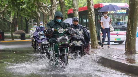 Mit Regencapes pflügen Menschen auf ihren Motorrädern durch die Fluten in Shanghai.