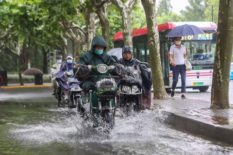Mit Regencapes pflügen Menschen auf ihren Motorrädern durch die Fluten in Shanghai.