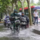 Mit Regencapes pflügen Menschen auf ihren Motorrädern durch die Fluten in Shanghai.
