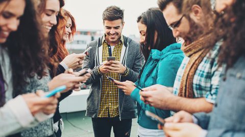 Gruppe von Freunden steht zusammen, jeder schaut auf sein Handy und freut sich über neue Deals ohne Anschlusspreis.