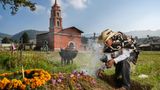 World Press Photo: Ein mit Hut und Poncho gekleideter Mann mit Räuchergefäß an einem mit Blumen geschmückten Grab.