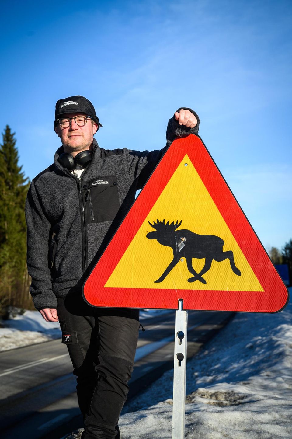 Johan Erhag, Miterfinder und Projektleiter der Elch-Show in Schweden, mit einem Straßenschild, das vor Elchen warnt Johan Erhag, Miterfinder und Projektleiter der Elch-Show in Schweden, mit einem Straßenschild, das vor Elchen warnt