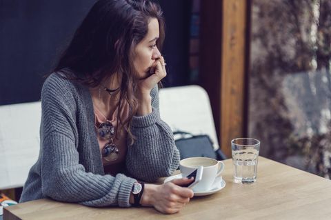 Eine junge Frau sitzt nachdenklich am Tisch