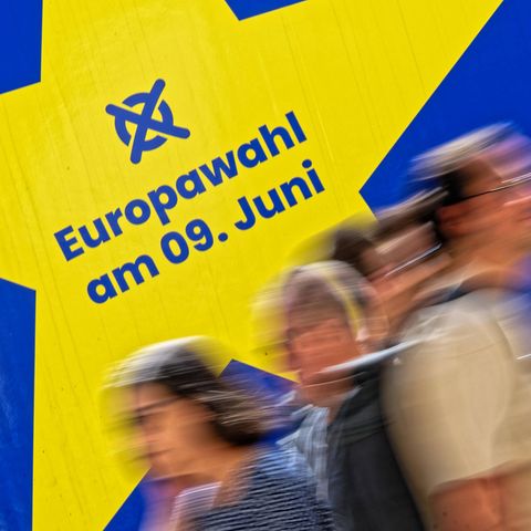 Verschwommene Menschen laufen vor einem Schild zur Europawahl am 9. Juni vorbei.