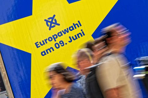 Verschwommene Menschen laufen vor einem Schild zur Europawahl am 9. Juni vorbei.