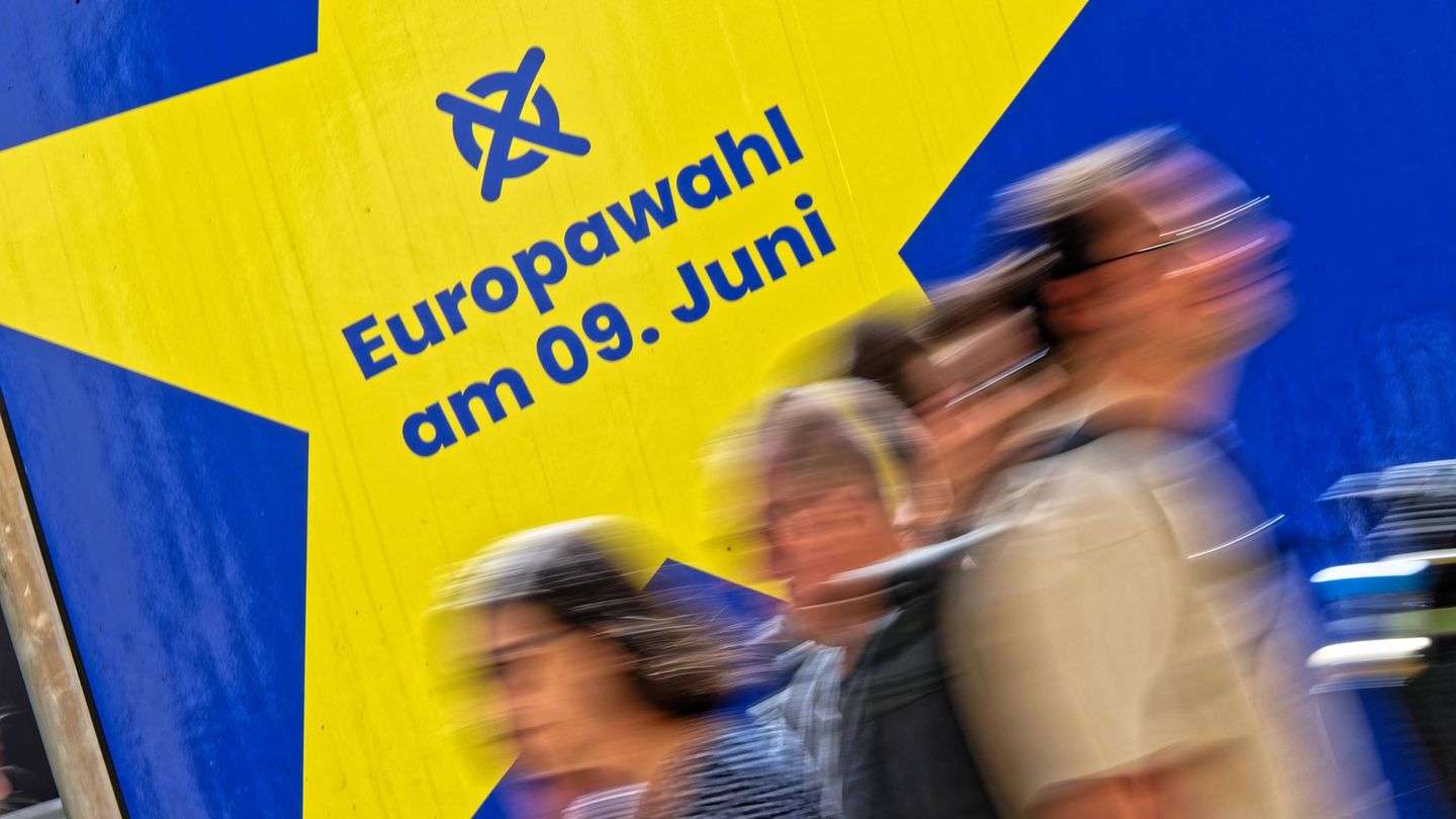 Verschwommene Menschen gehen an einem Schild zur Europawahl am 9. Juni vorbei.