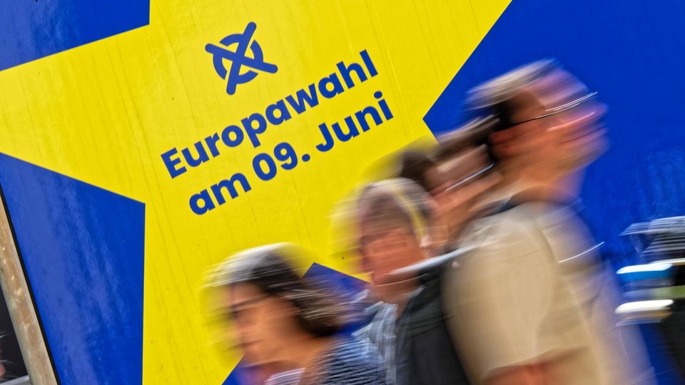 Verschwommene Menschen laufen vor einem Schild zur Europawahl am 9. Juni vorbei.