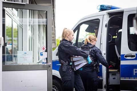 Polizeibeamtinnen gehen während einer Durchsuchung mit Ordnern an einem Polizeiwagen vorbei