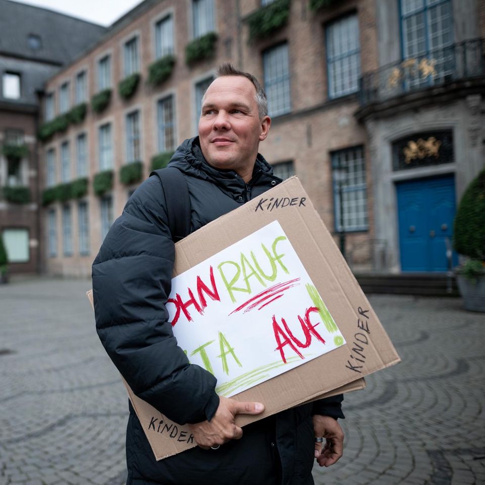 Alex Liefermann steht mit Plakat auf Marktplatz in Düsseldorf