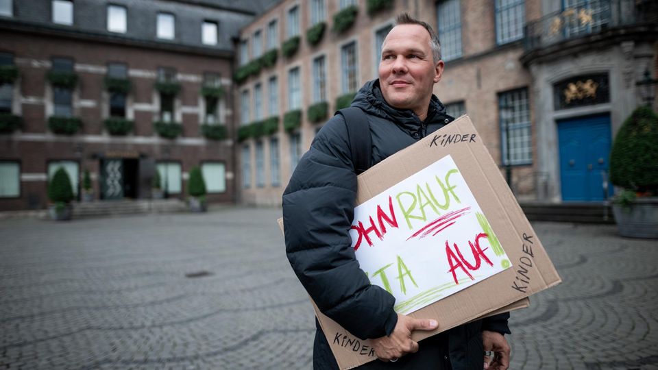Alex Liefermann steht mit Plakat auf Marktplatz in Düsseldorf