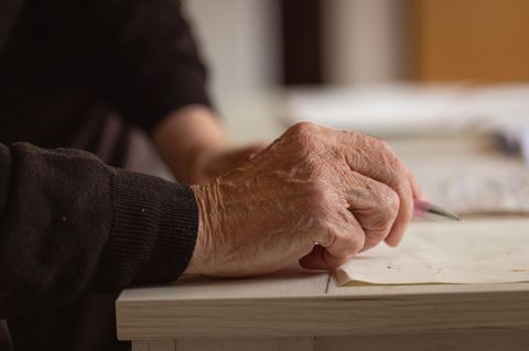 Die rechte Hand eines alten Mannes hält einen Kugelschreiber über ein weißes Blatt Papier